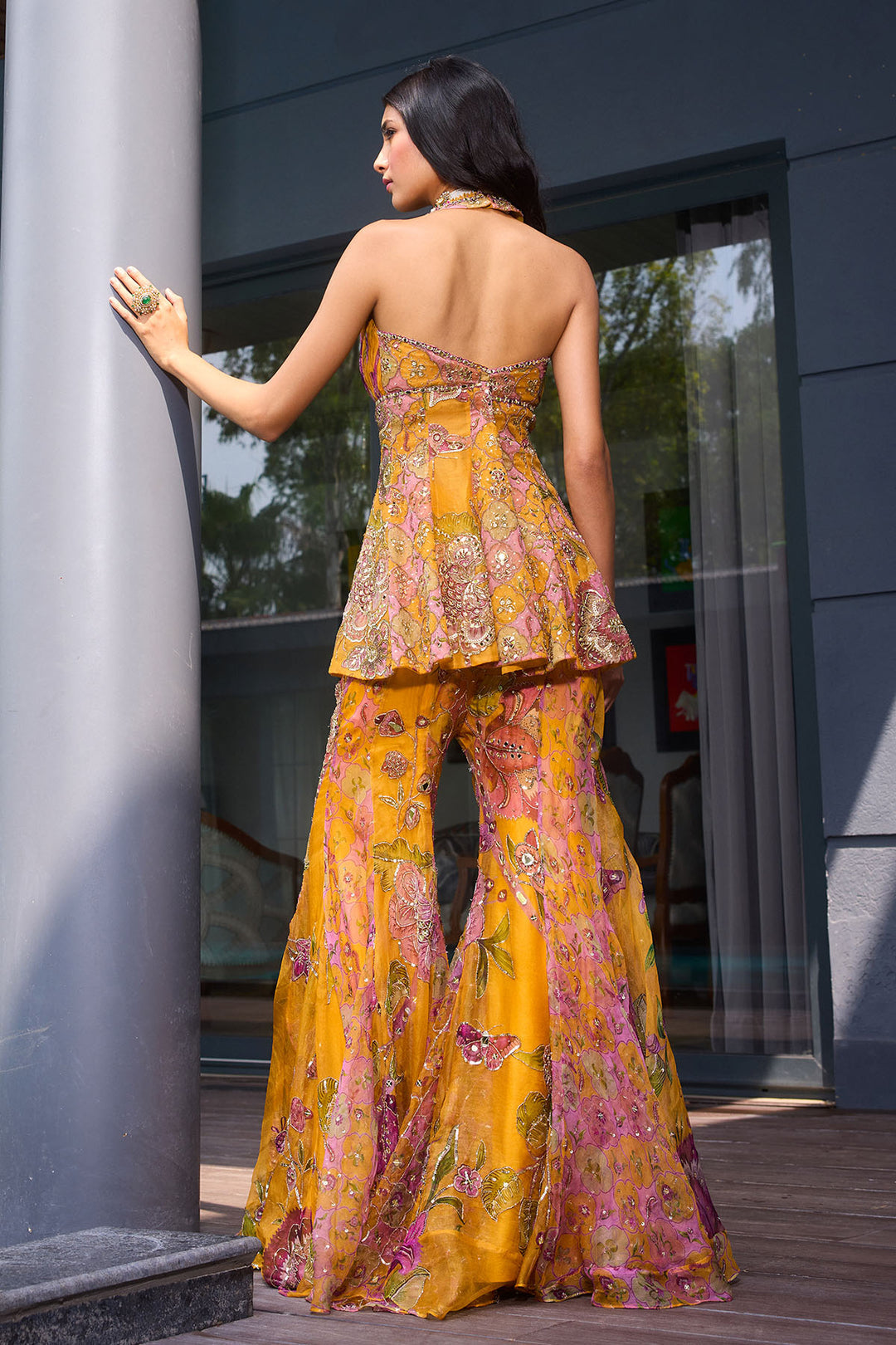 Woman in a yellow floral dress standing outdoors near a building entrance.